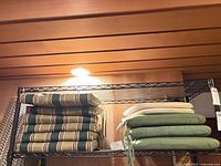 Stack of six striped cushions and five mixed green/beige cushions on shelving
