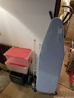 Ironing board, drying rack, two stacked storage tubs with red lids