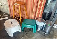 Group shot of wood stool, white and green step stools, two stainless pedal trash cans
