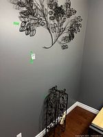 Wall-mounted metal leaf sculpture above black wrought iron wine rack containing decorative bottle