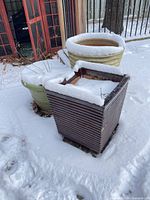 Three planters in snow: slatted wood square, green round, yellow ribbed round
