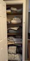 Full closet view with folded towels and bedding on four shelves