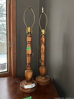 Pair of turned wood table lamps standing on surface showing overall form