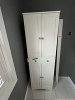 Full view of white freestanding bathroom cabinet showing doors and drawer