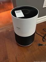 Front view of Winix air purifier showing white body, black perforated base, black vented top, attached power cord