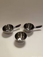 Three stainless vessels, two with rosewood handles, one plain bowl