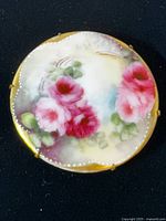 Front view of round Limoges enamel brooch showing pink rose motif and dotted border