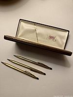 Three gold-tone Cross pens and brown Cross case