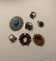 All seven jewellery pieces laid out: three rings, three brooches, one pendant