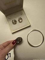 All three jewellery pieces laid out: sterling bangle, hoop earrings in box, amethyst ring held by hand