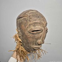 Frontal view of carved wood mask with raffia, showing facial features