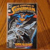 Front cover of The Adventures of Superman #447 inside bag with board on wood surface