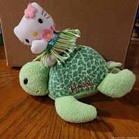 Front view of Hello Kitty riding turtle plush showing facial features and embroidered Aloha text