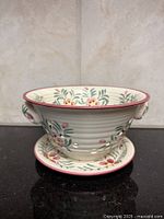 Side view of berry bowl on underplate showing floral motif and holes