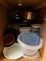 Cabinet shelf showing stack of clear plastic containers and assorted lids