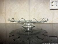 Side profile of clear glass pedestal cake stand showing scalloped rim and pedestal base