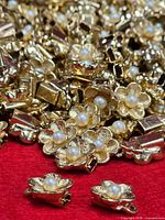 Pile of gold-tone floral charms with faux pearls on red background