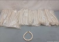 Six sealed dozen-count bags of white pearl bracelets plus one sample bracelet displayed