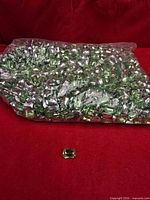 Large plastic bag filled with green faceted acrylic gems displayed on red background