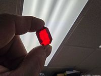 Hand holding single red plastic faceted piece against light showing shape and translucency