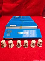 row of six porcelain thimbles in front of stack of blue Keepsakes boxes