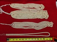 Four bundles of multiple pearl strands with measuring tape showing length