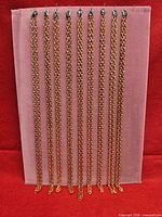 Nine copper-tone chain necklaces displayed vertically on board
