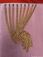 Nine copper-tone chain necklaces displayed on board