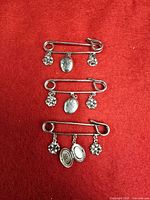 All three silver-tone charm brooches displayed on red background