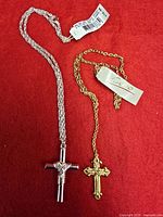 Both Coro cross necklaces displayed on red background