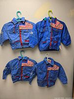 Front view of four identical blue denim children’s jackets with American flag patches and hangers