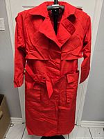 Front view of red trench coat on hanger showing double-breasted buttons, belt, pockets