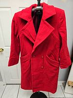 Front view of red wool coat on hanger showing buttons, pockets, collar