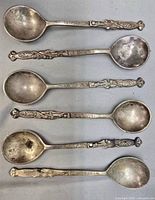 Front view of six ornate souvenir spoons showing dragon handles and Greek-key borders