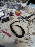overview of table with bin of mixed jewellery, various necklaces, bracelets and accessories visible