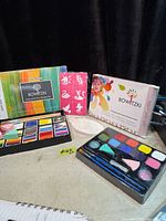 Both Bowitzki face paint kits displayed with trays of paints, brushes, sponges and stencil sheet visible