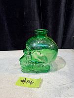 Side profile of green glass skull bottle showing molded facial features