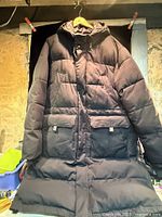 Full front view of dark quilted parka on hanger showing overall style and condition