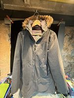 Front view showing grey parka, faux-fur hood, zipper, pockets