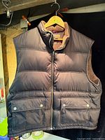 Front view of brown quilted winter vest on hanger showing zipper and pockets