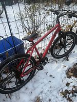 Full view of red Mongoose bicycle leaning against fence in snow