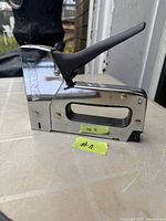 Side view of chrome RONA manual staple gun showing handle and staple exit