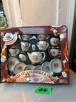 Front of boxed 15-piece porcelain tea set, shows all pieces and floral design