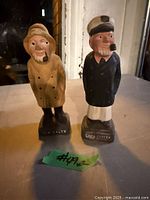 Front view of both ceramic nautical shakers showing figures, base labels, overall condition
