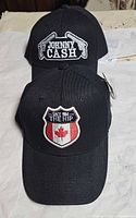 Both black baseball caps showing front embroidery, Johnny Cash and The Hip designs