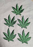 Five identical green cannabis leaf shaped embroidered patches laid flat