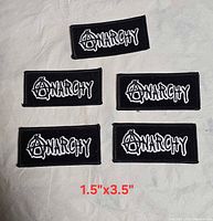 Five identical black embroidered Anarchy patches laid out on surface, size text overlay 1.5" x 3.5"