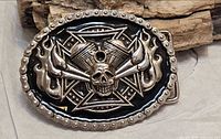 front view of oval buckle showing skull, engine, flame design, black enamel, studded rim