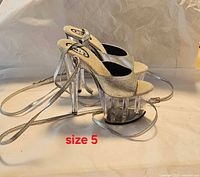 Side view of both sandals showing clear heels, silver uppers, ankle straps