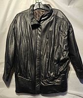 Front view of black leather jacket on hanger showing pleated design and pockets